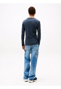 Navyblauw shirt met lange mouwen en een ronde hals, gecombineerd met ontspannen lichtblauwe denim cargobroeken met zijzakken. Casual schoeisel zichtbaar.