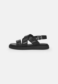 Black leather sandals with crossed straps, adjustable ankle buckle, flat sole, and minimalist design. Smooth texture with matte finish.