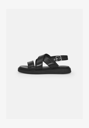 Sandali in pelle nera con cinturini incrociati, fibbia regolabile alla caviglia, suola piatta e design minimalista. Texture liscia con finitura opaca.