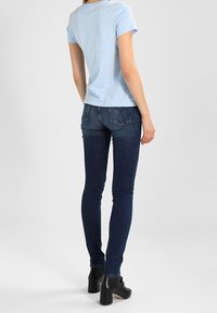 Vaaleansininen puuvillapaita lyhyillä hihoilla, yhdistetty tummansiniset kapeat farkut ja mustat korkeat nilkkasaappaat.