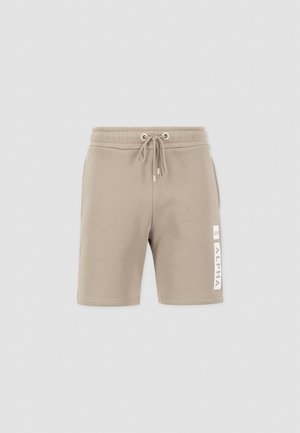 Pantalones cortos en un tono beige claro, hechos de una tela suave, con una cinturilla elástica y cordones, y un detalle de logotipo blanco en la pierna izquierda.