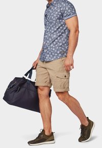 Maglietta casual a maniche corte blu con motivo, pantaloni cargo color khaki e sneakers olive; con una borsa a tracolla scura con dettagli blu.