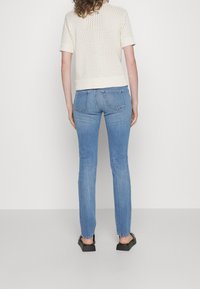 Lättstickad krämfärgad topp med korta ärmar, tillsammans med smala blå jeans som har bakfickor och längd till anklarna. Svarta skor.