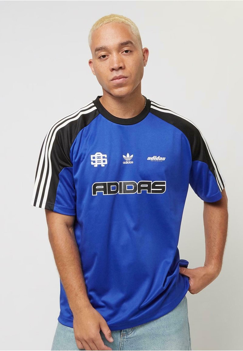 Blå Adidas-tröja med svarta axlar, vita ränder och en stor svart "ADIDAS"-logotyp. Slät tyg, sportig design, kortärmad.