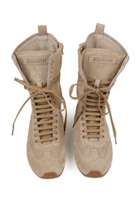Sneakers high-top in suede beige con punta arrotondata, lacci piatti e occhielli in metallo. Branding visibile sulla linguetta imbottita. Suola in gomma.