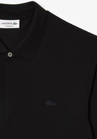 Schwarzes Lacoste-Poloshirt mit strukturierter Webart, klassischem Kragen, Zwei-Knopf-Leiste und kleinem, gesticktem Logo auf der linken Brust.
