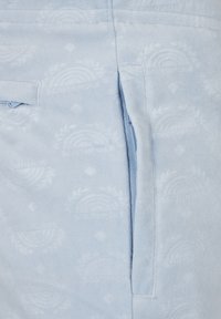 Světlounce modrá fleecová látka s vyraženými vzory ve tvaru duhy. Má viditelnou boční kapsu se zapínáním na zip. Měkká textura.