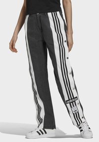 Svarta denimbyxor med vita sidosträck, tryckknappar och en Adidas-logotypen. Har en rak ben-design och en klassisk passform.