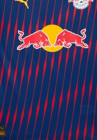 Puma fodboldtrøje med blåt stof og røde lodrette striber, Red Bull-logo og en gul cirkel. Authentic Football-label nederst.