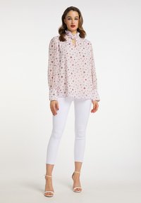 Blomstermønstret bluse i blød lyserød stof med en nøglehulshals, lange puffærmer og hvide skinny bukser med ankelremme.