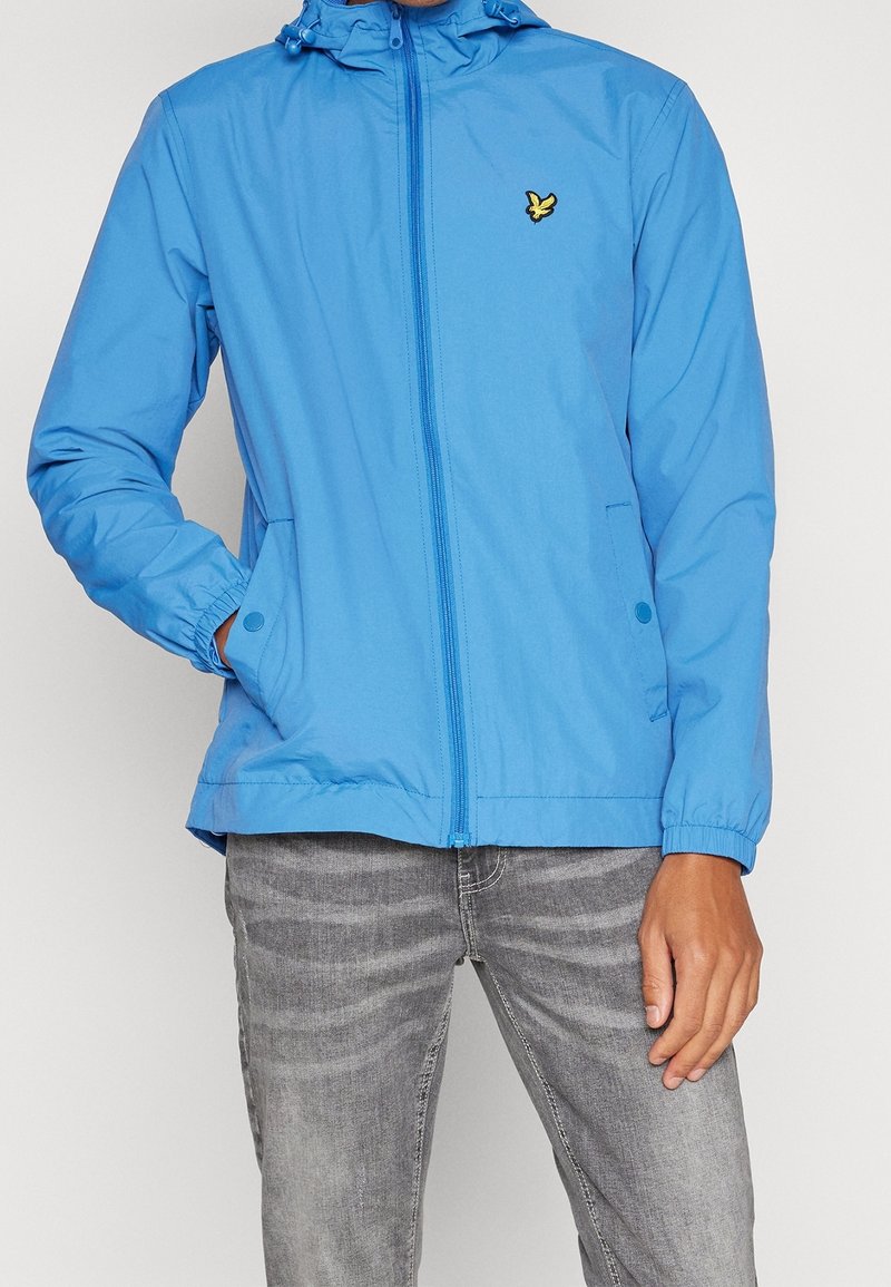 Light blue zip-up jacket with a hood, elastic cuffs, and two side pockets. Features a small yellow logo on the left chest area.