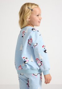 Light blue sweatshirt featuring playful penguin designs in pink and red hats, with a soft, fleece-like texture and elastic cuffs.