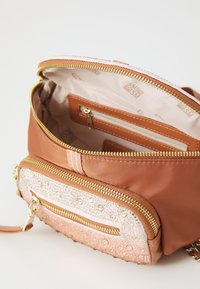 Sac à main de couleur orange avec un extérieur lisse, présentant une poche avant texturée et embellie ainsi que des détails de fermeture éclair en or. S'ouvre sur un intérieur doublé.