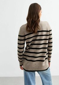 Beige tröja med svarta horisontella ränder, som har en mjuk textur och en något längre bakre fåll. Bärs med ljusblå jeans.