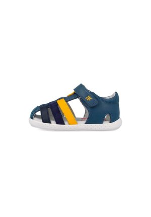 Sandalia para niño pequeño en azul y amarillo con suela blanca, talón cerrado y correa ajustable de Velcro sobre fondo blanco.