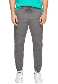 Man som bär grå joggerbyxor med dragsko i midjan och elastiska muddar, tillsammans med vita sneakers och vita strumpor.