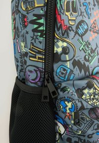 Mochila negra y gris con patrones gráficos coloridos, que presenta cremalleras con tiradores cuadrados, un bolsillo lateral de malla y diseños caricaturescos distintivos.