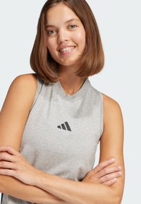 Sivi bezrukavi sportski top od mekanog materijala, s okruglim izrezom i crnim logotipom sprijeda. Glatka tekstura, ležeran dizajn.