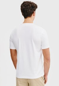 Biała koszulka z krótkim rękawem, wykonana z gładkiej bawełnianej mieszanki, z klasycznym okrągłym dekoltem i regularnym krojem. Brak widocznych wzorów lub akcentów.