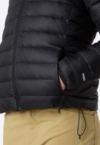 Svart puffjacka med horisontella sömmar, fickor med dragkedja och justerbara dragsko i midjan. Tyget ser slätt och vattenavvisande ut.