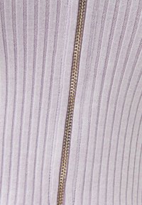 Tejido de lavanda acanalado con un destacado detalle de cremallera dorada que corre verticalmente por el centro, mostrando una superficie texturizada.