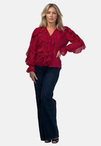 Czerwona bluzka z szyfonu z falbaniastymi detalami, dekoltem w serek i długimi rękawami. Połączona z ciemnymi spodniami dzwonami i czarnymi sandałami na obcasie.