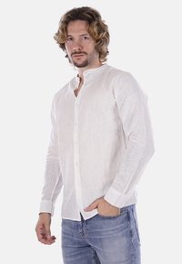Camicia bianca in lino con maniche lunghe, chiusura a bottoni e colletto alla coreana; abbinata a jeans in denim blu. Texture liscia, design leggero.