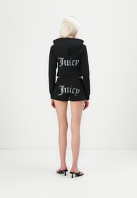 Crni skraćeni dukserica i šorts set s srebrnim "Juicy" grafikom. Glatka tekstura, ležeran kroj i opušteni dizajn s kapuljačom.
