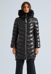 Melns pūkains mētelis ar chevron rakstu, spīdīgu tekstūru, ar kažokādas apdari pie kapuces, aizmugurē ar rāvējslēdzēju un sānu kabatām.