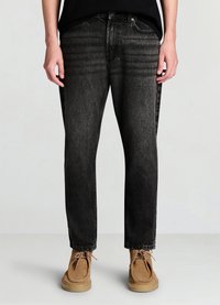 Schwarze Jeans aus Denim mit geradem Schnitt, Akzenten durch Waschungseffekte und Fünf-Taschen-Design, kombiniert mit hellbraunen Wildlederschuhen.