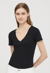 T-shirt nera a maniche corte con scollo a V, realizzata in tessuto morbido, caratterizzata da un design aderente e una texture liscia, abbinata a pantaloni in denim bianchi.