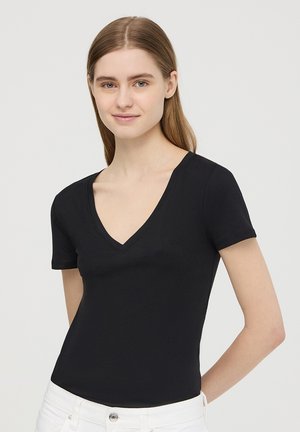 T-shirt nera a maniche corte con scollo a V, realizzata in tessuto morbido, caratterizzata da un design aderente e una texture liscia, abbinata a pantaloni in denim bianchi.