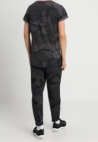 Set s černým kamuflážním vzorem, skládající se z krátkého rukávu a kalhot, vyrobený z prodyšné tkaniny, s texturovanými akcenty a volným střihem.