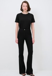 Zwarte top met korte mouwen en een bewerkte halslijn, gecombineerd met hoge zwarte flared broek. Model draagt zwarte hakken.