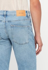 Jasnoniebieskie dżinsy z fakturowanym wykończeniem, z skórzaną naszywką z napisem "ONLY & SONS" na plecach oraz dwiema tylnymi kieszeniami.
