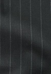 Tissu noir avec un motif en chevrons et des rayures blanches contrastantes. La texture semble lisse et tissée.