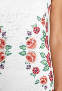 Tessuto di pizzo bianco con vivaci ricami floreali in rosso, arancio e verde, caratterizzato da dettagli intricati e texture in tutto il materiale.