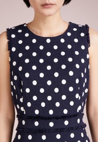 Námořnická bezramínková blůza s bílými puntíky, texturovaná tkanina a třepené okraje podél ramenních švů a pasu.