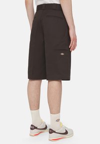 Mørkebrune cargo shorts med sidelommer og et logo-patch, med en afslappet pasform og robust stof. Designet til holdbarhed og komfort.
