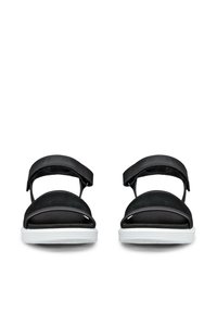 Par de sandalias negras de punta abierta con correas ajustables en el tobillo y suelas acolchadas blancas, mostradas desde el frente sobre un fondo blanco.