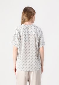 Haut à manches courtes, col rond en tissu léger avec un motif géométrique noir et blanc, présentant un bouton unique au dos.