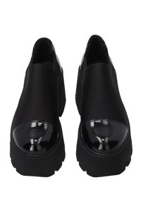 Pár černých slip-on platformových bot s lesklými patentovými špičkami a silnými robustními podrážkami, zobrazené zepředu.