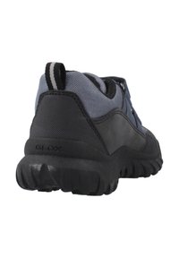 Zapatilla negra y gris con una suela de goma texturizada, parte superior de malla y cuello acolchado. Presenta una lengüeta y un logo sutil en el lateral.