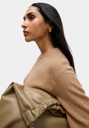 Maglione beige con scollo rotondo indossato da una persona che tiene una grande borsa in pelle taupe morbida con design arricciato e dettagli in metallo dorato.