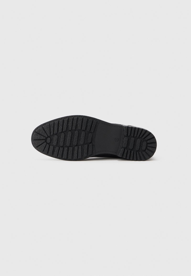 Suela de zapato negra con un patrón de relieve profundo y agarre texturizado, exhibida de forma plana sobre un fondo blanco.