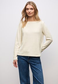 Cremefarbener Pullover aus weichem Stoff, mit einem Bootsausschnitt und langen Ärmeln. In Kombination mit blauen Jeans hat er eine lässige Passform.