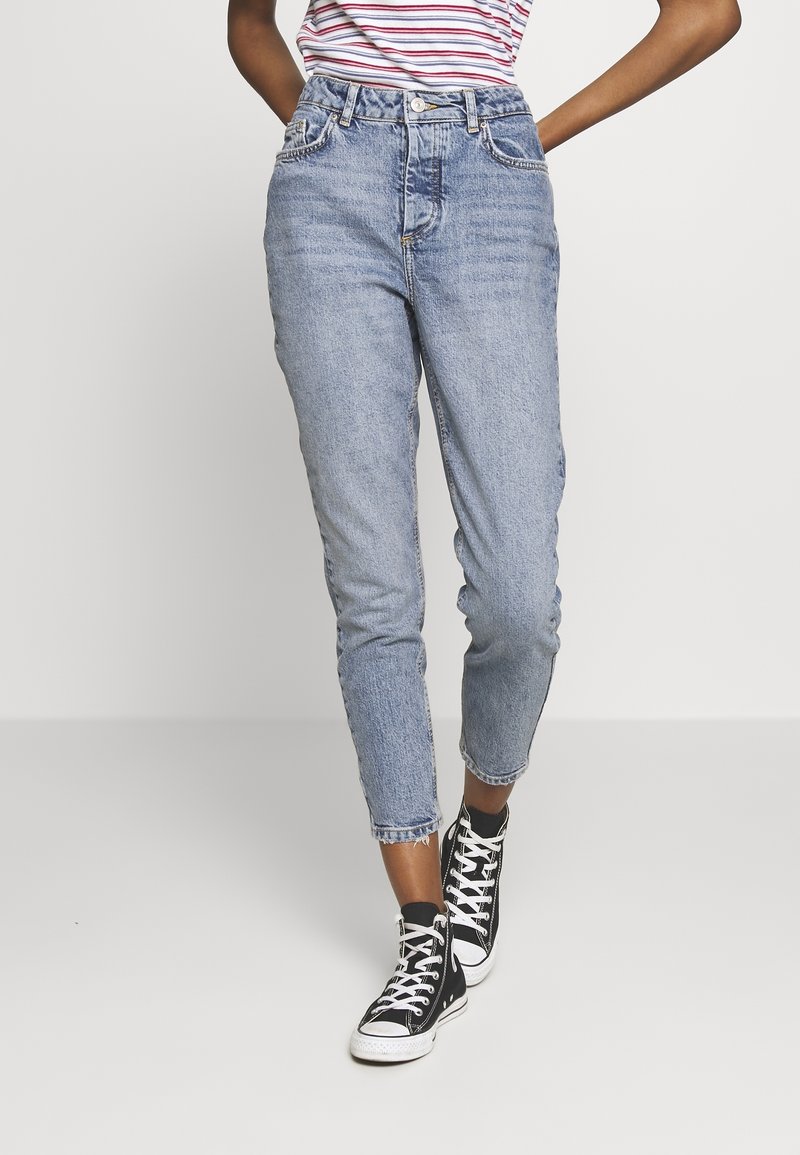 Světle modré, jeansy s vysokým pasem a volným střihem, s vybledlým vzhledem a třepeným lemem. V kombinaci s černými vysokými teniskami.