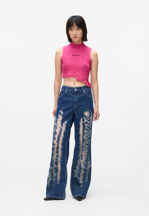 Top in maglia corto rosa con collo alto, abbinato a jeans in denim a gamba larga strappati con ampi ritagli verticali. Scarpe nere con punta a punta.