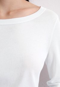 Maglietta bianca a maniche lunghe con scollatura ampia, texture liscia, colletto a costine e maniche aderenti, che mette in mostra un design minimalista.