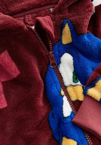 Maroon fleece hoodie featuring a blue graphic design, a zipper closure, and ribbed cuffs. Soft texture with vibrant color accents.